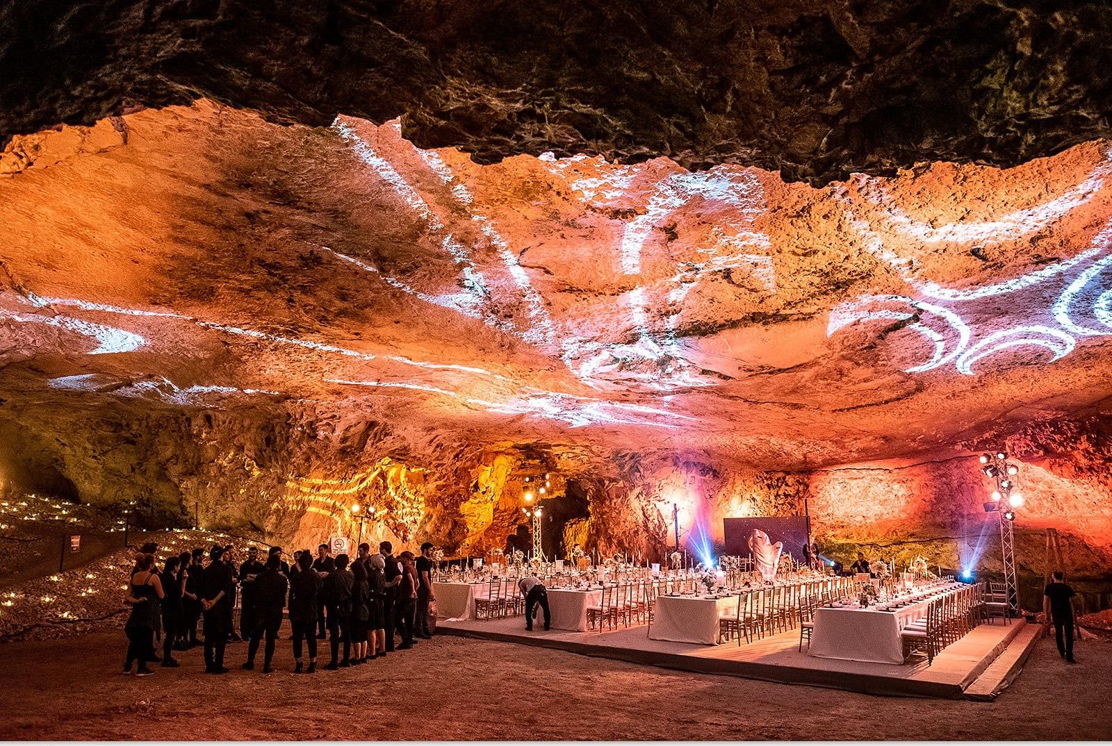A long dinner table set inside a lit cave, the crew lined up before guests arrive