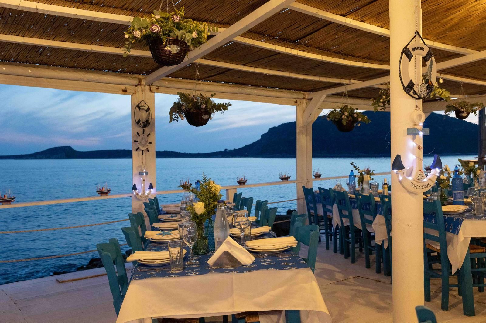 A seaside taverna terrace set for dinner at dusk, Greece